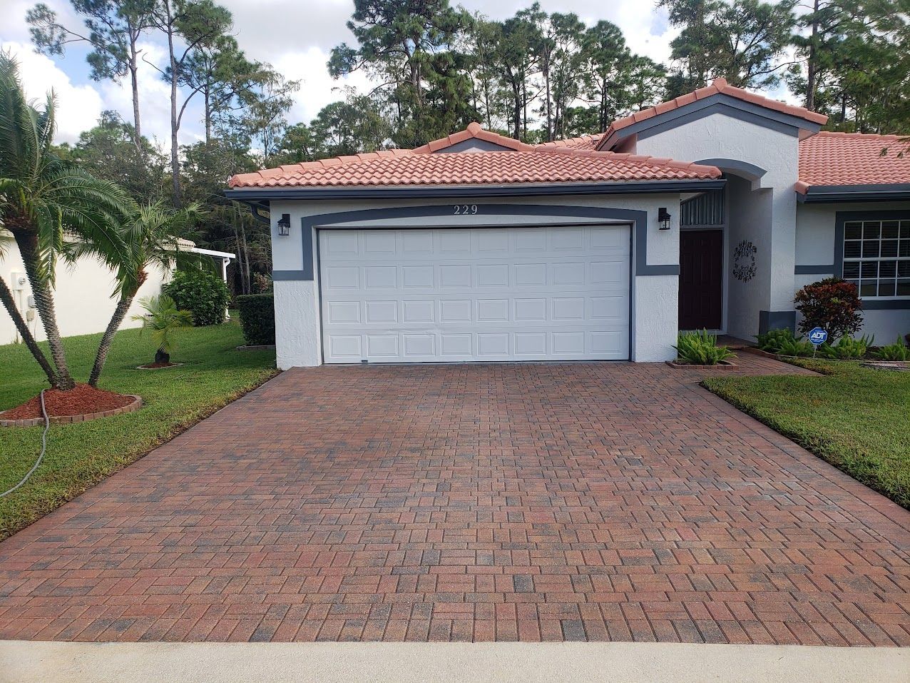 Brick driveway leading to a white garage on a suburban house with red tile roof and green lawn