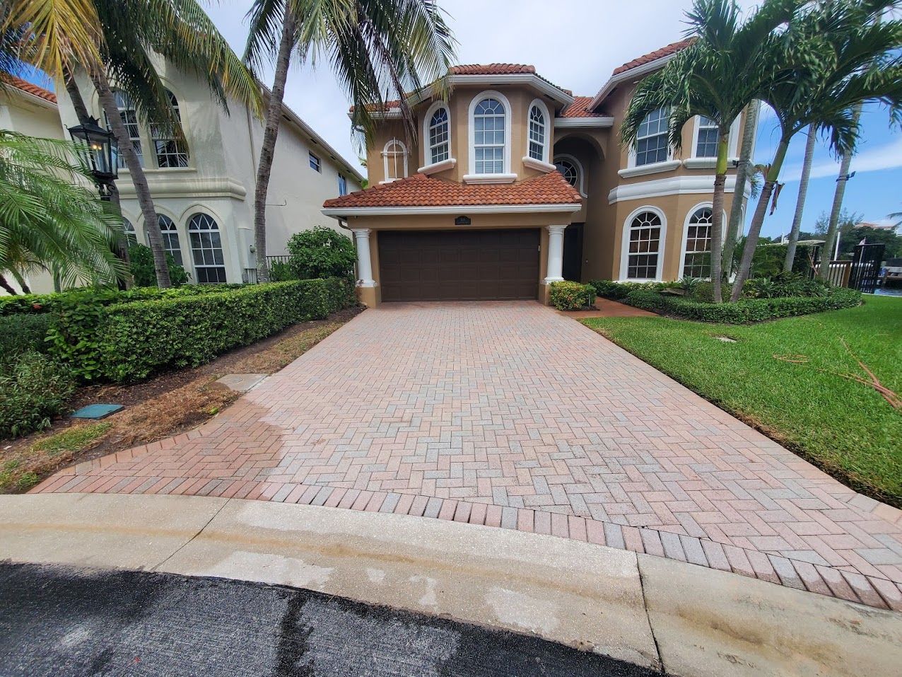 Brick driveway leading to a Mediterranean-style house with palm trees and a red tile roof