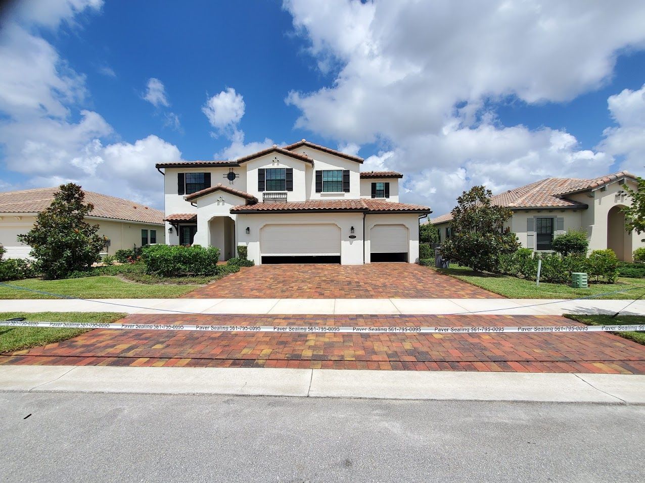 Two-story suburban house with white garage, red-tile roof, and a brick driveway under a blue sky.
