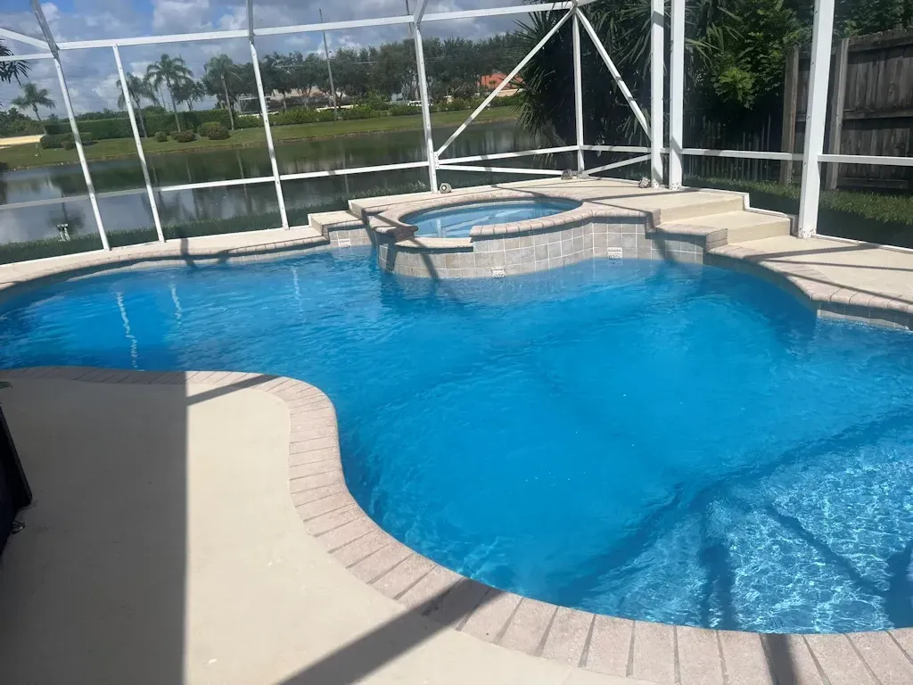 Backyard swimming pool with blue water, curved tan deck, and screened enclosure under a sunny sky