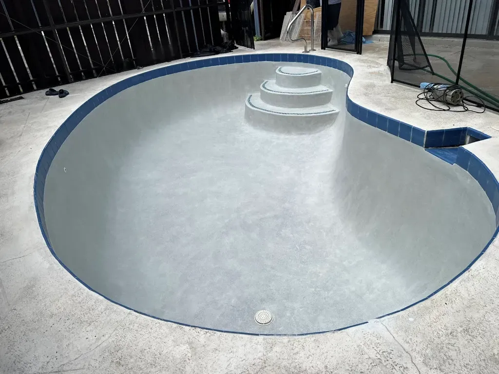 Empty drained swimming pool with a curved blue edge and white steps inside.