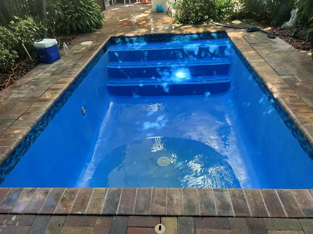 Blue rectangular backyard swimming pool with brick border and surrounding patio greenery