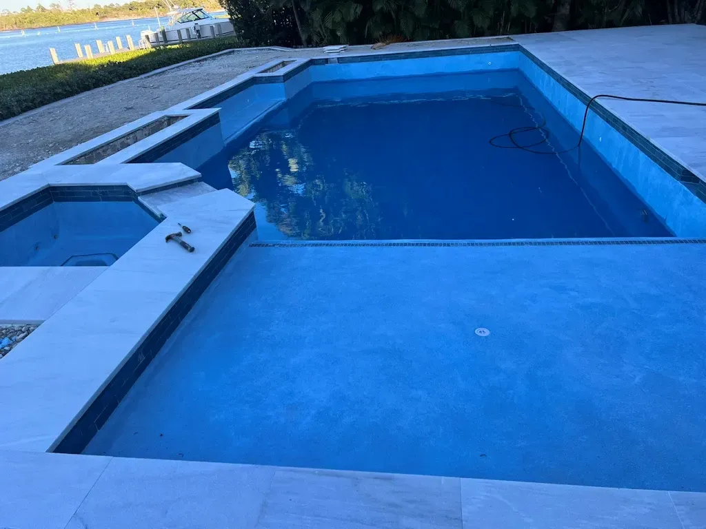 Blue backyard pool with a shallow ledge and surrounding stone patio at dusk