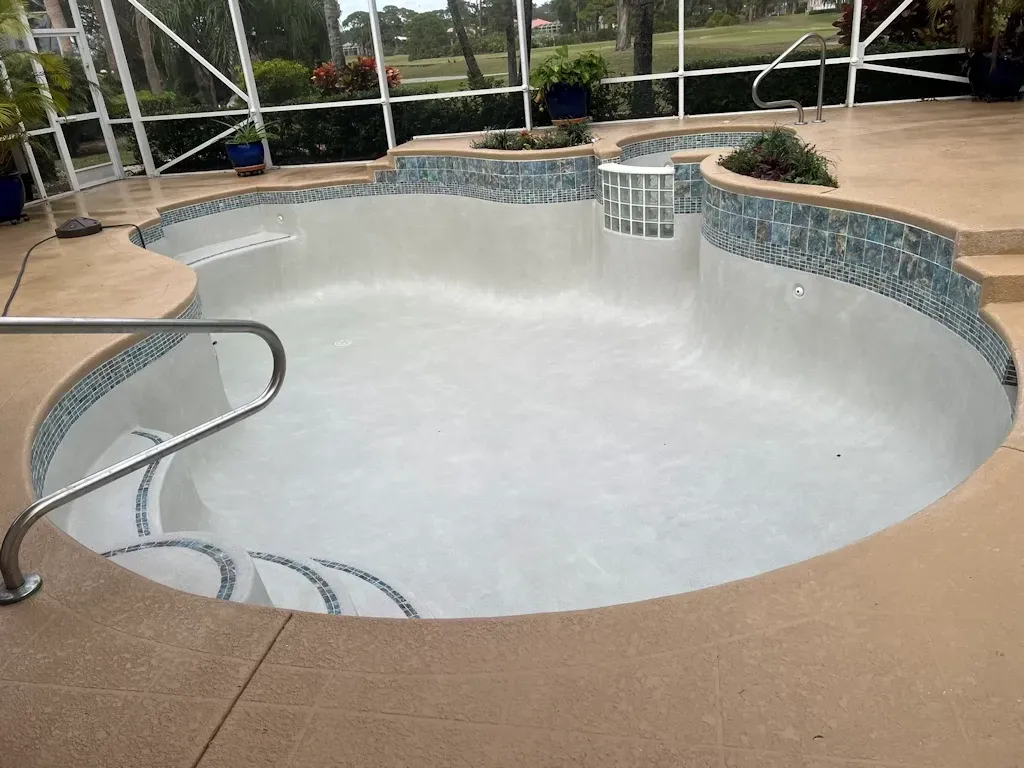Empty white pool with curved spa, tan deck, and stainless steel handrail indoors