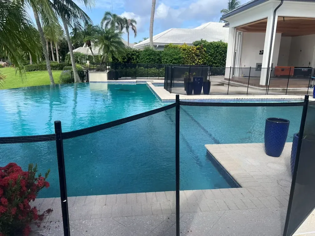 Backyard pool with turquoise water, black safety fence, and patio seating beside a house