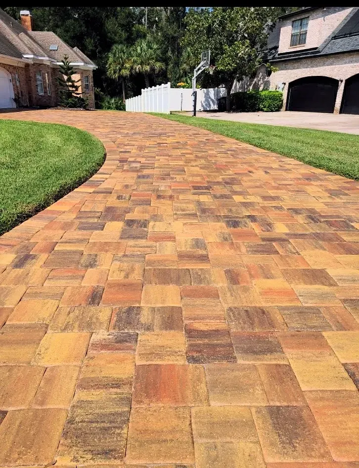 Brick-paved driveway curving toward a house, bordered by green lawns and garage doors