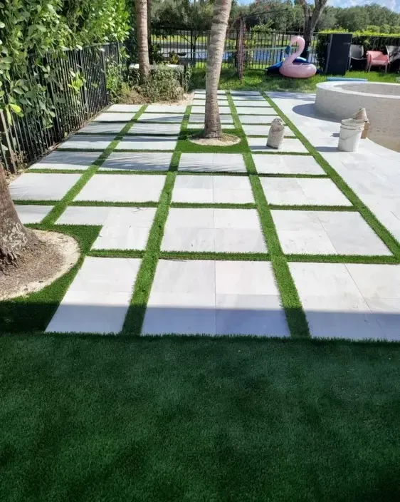 Modern backyard walkway with white stone pavers, green grass joints, palm trees, and lawn edging