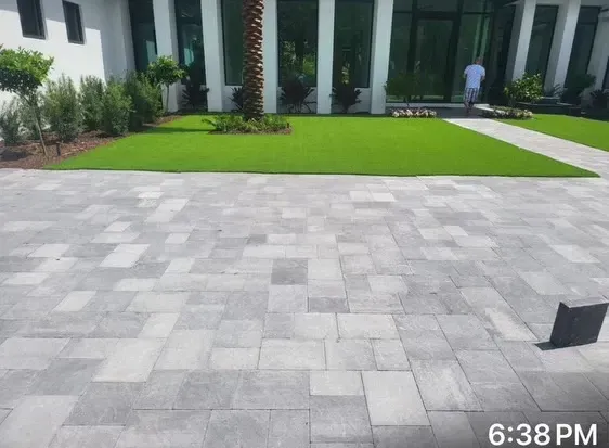 Gray tiled patio with a bright green lawn and modern building columns in the background at dusk