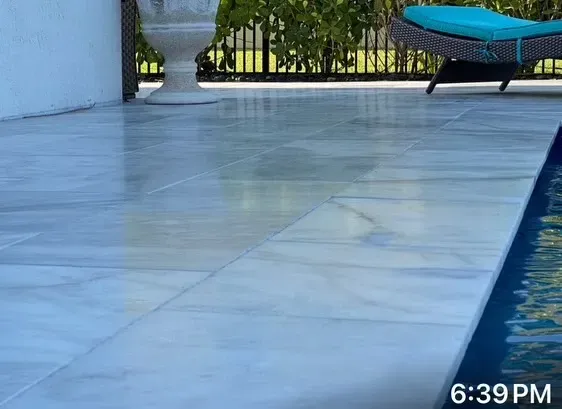 Poolside patio with wet tile, blue lounge chair, and black railing at dusk