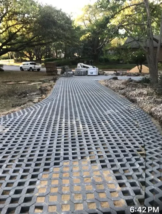 Grid pavers installed on a curved garden path with rocks and trees nearby, a car parked in the background.