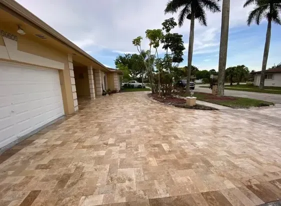 Empty tiled driveway beside garages with palm trees and a cloudy sky