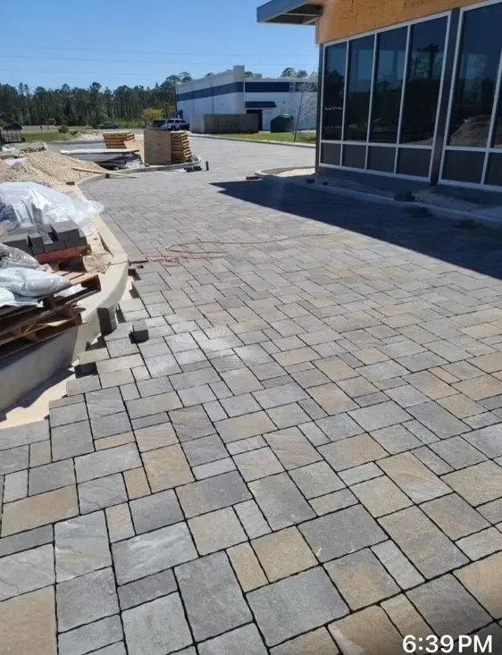 Paved courtyard beside a glass-front building, with stacked materials and construction supplies nearby.