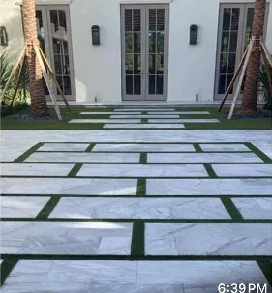 Modern front walkway of white stone slabs set in grass leading to French doors and palms.