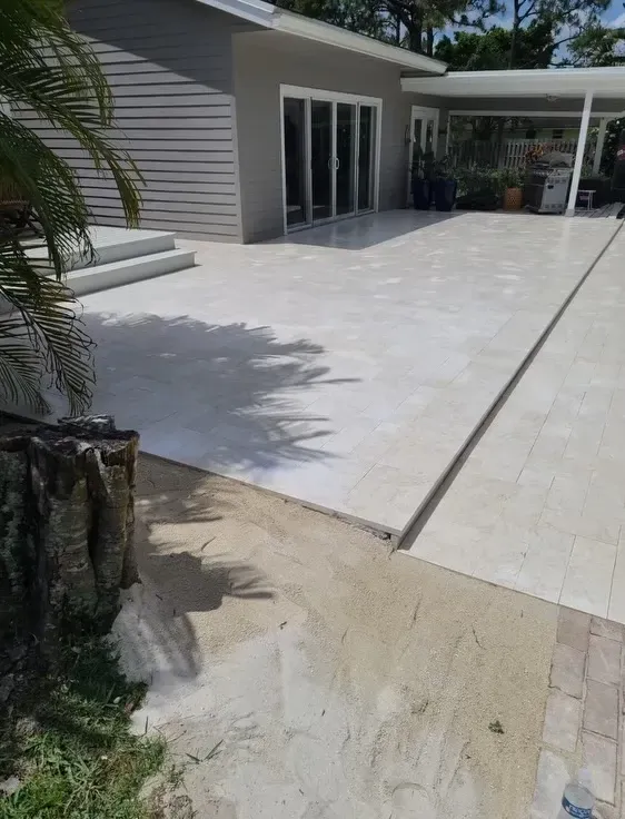 Modern house patio with large light-gray tiled terrace and sliding glass doors beside a covered walkway