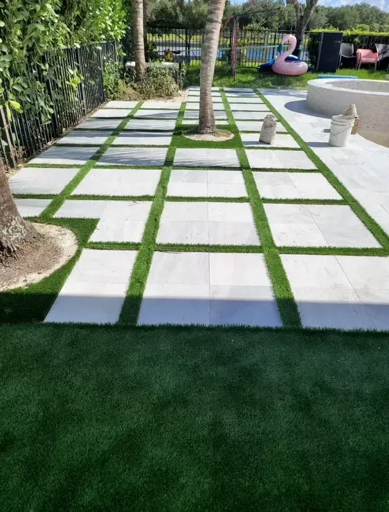 Modern garden walkway with square stepping stones, green grass joints, trees, and patio seating nearby