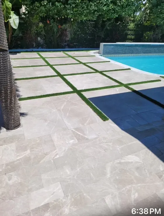 Poolside patio with light stone tiles, green grass joints, and a blue swimming pool at sunset