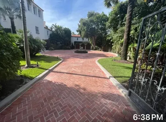 Brick walkway through landscaped courtyard with palm trees and white buildings at sunset.