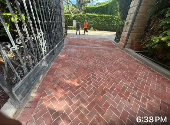 Brick driveway entrance with two people walking toward a green garden gate at dusk