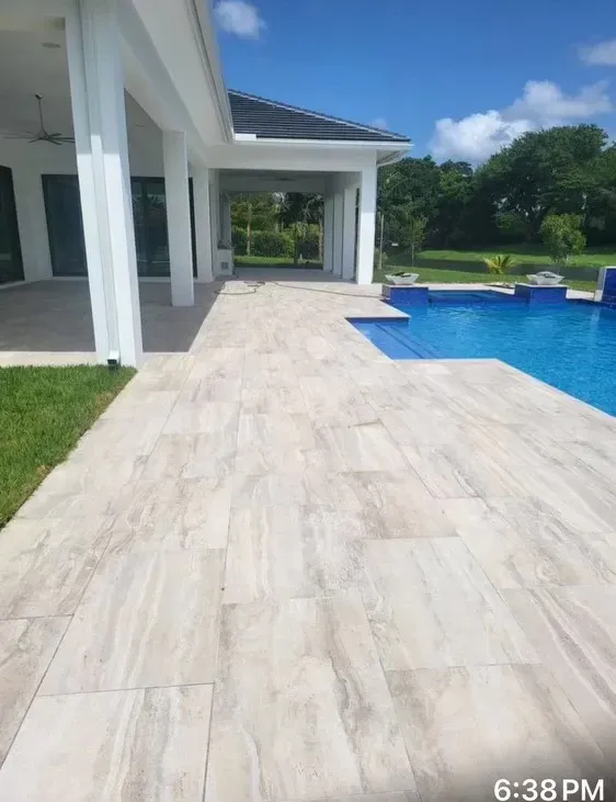 Modern patio beside a blue swimming pool, with white columns and a green lawn under a sunny sky.