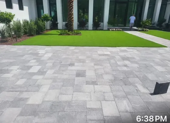 Modern courtyard with gray paving stones, green lawn, and building facade; person walking in the background.