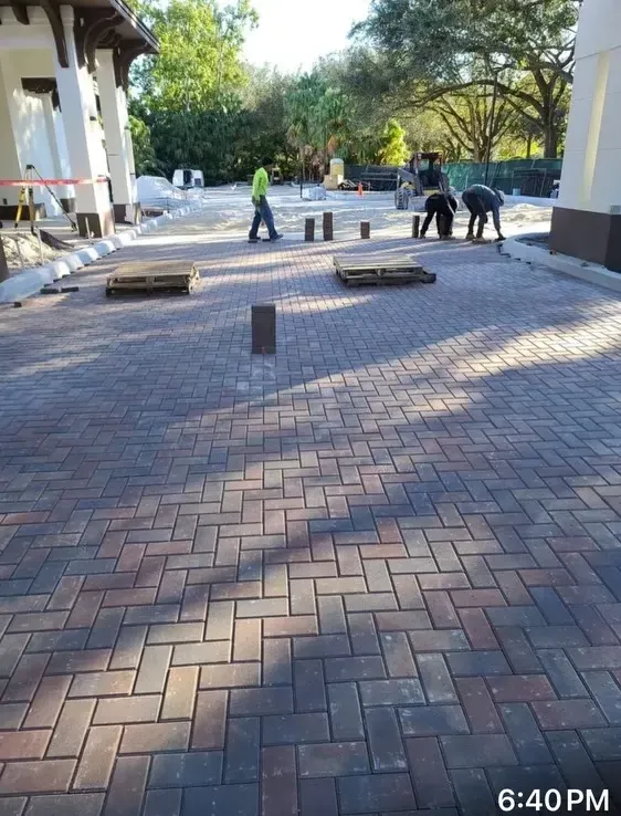 Workers installing bricks on a paved courtyard beside a building at dusk