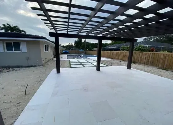 Covered backyard patio with white tile floor, dark pergola beams, and fenced yard beside a house