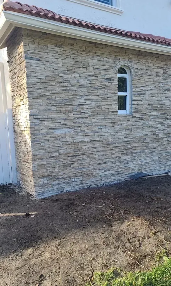 Stone exterior wall of a house with a small arched window and dirt ground in front