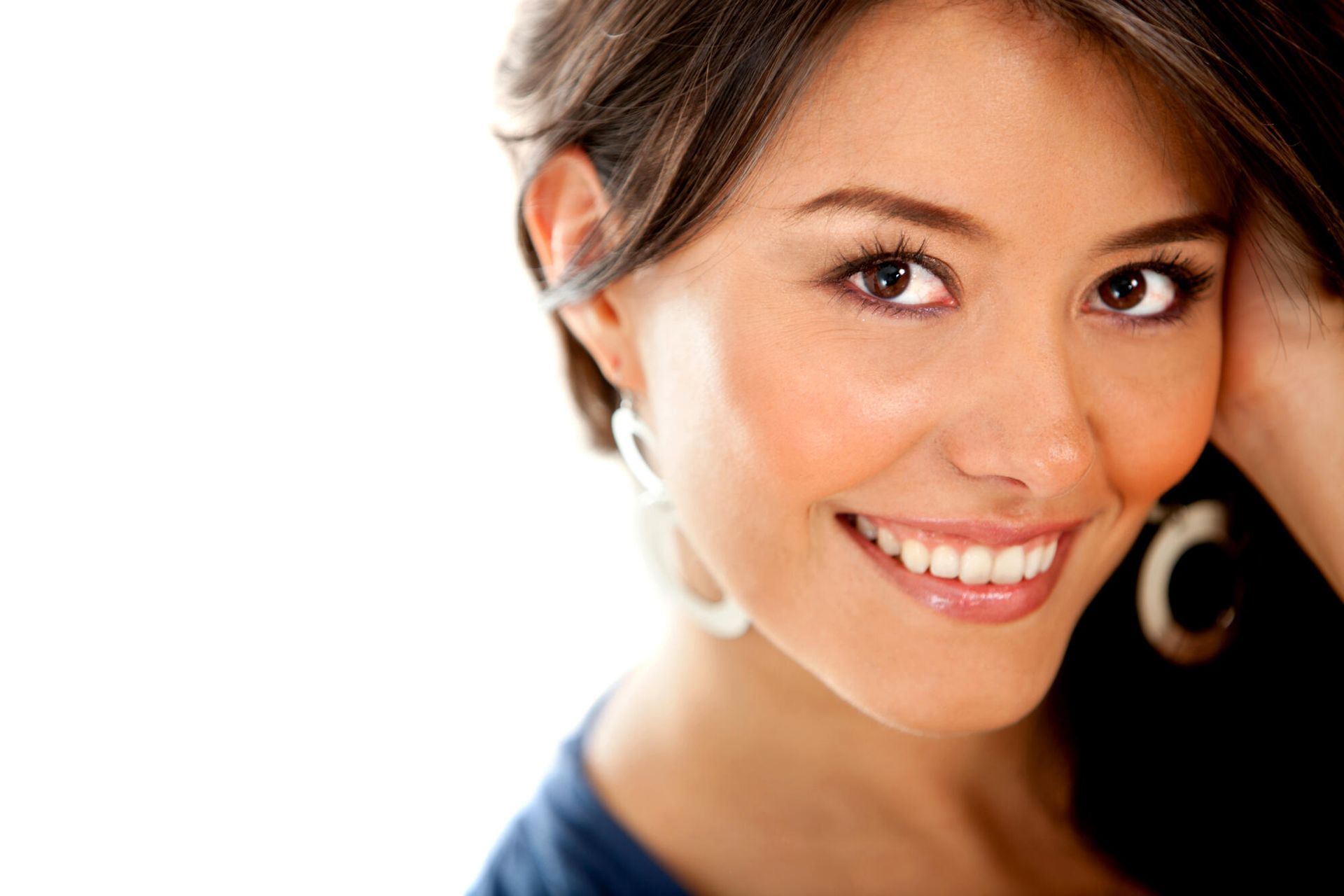 Woman smiles, looking toward the viewer; wearing large hoop earrings and a blue top; white background.