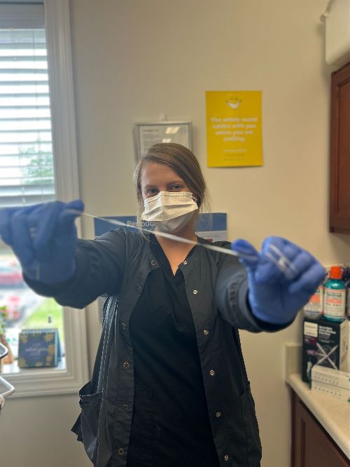 Una mujer con mascarilla y guantes azules sostiene una jeringa.