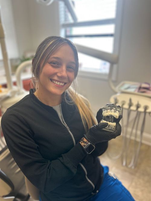 Una mujer está sentada en una silla dental sosteniendo un modelo de dientes.
