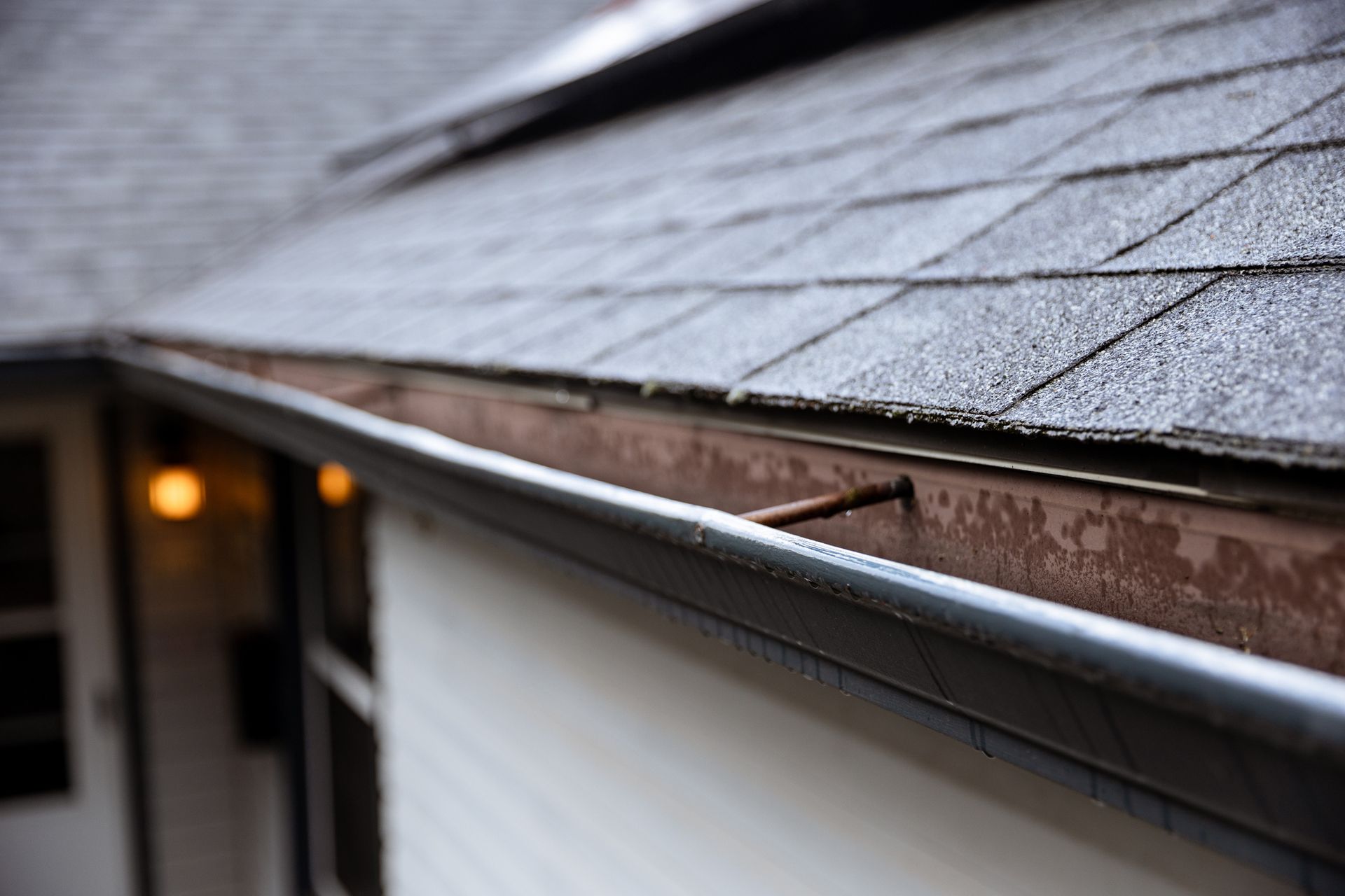 Close-up of a brown and gray roof with a gutter on a white house.