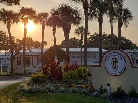 Sunrise over a palm-lined entrance sign and low buildings in a landscaped campus or resort setting