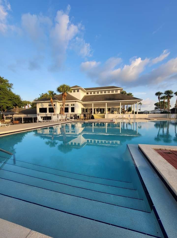Resort-style pool reflecting a white clubhouse under a blue sky at sunset