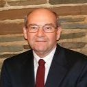 Man in glasses and suit with red tie, standing before a brick wall
