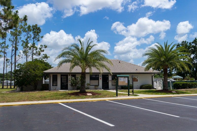 Single-story building with palm trees and empty parking spaces under a partly cloudy sky.