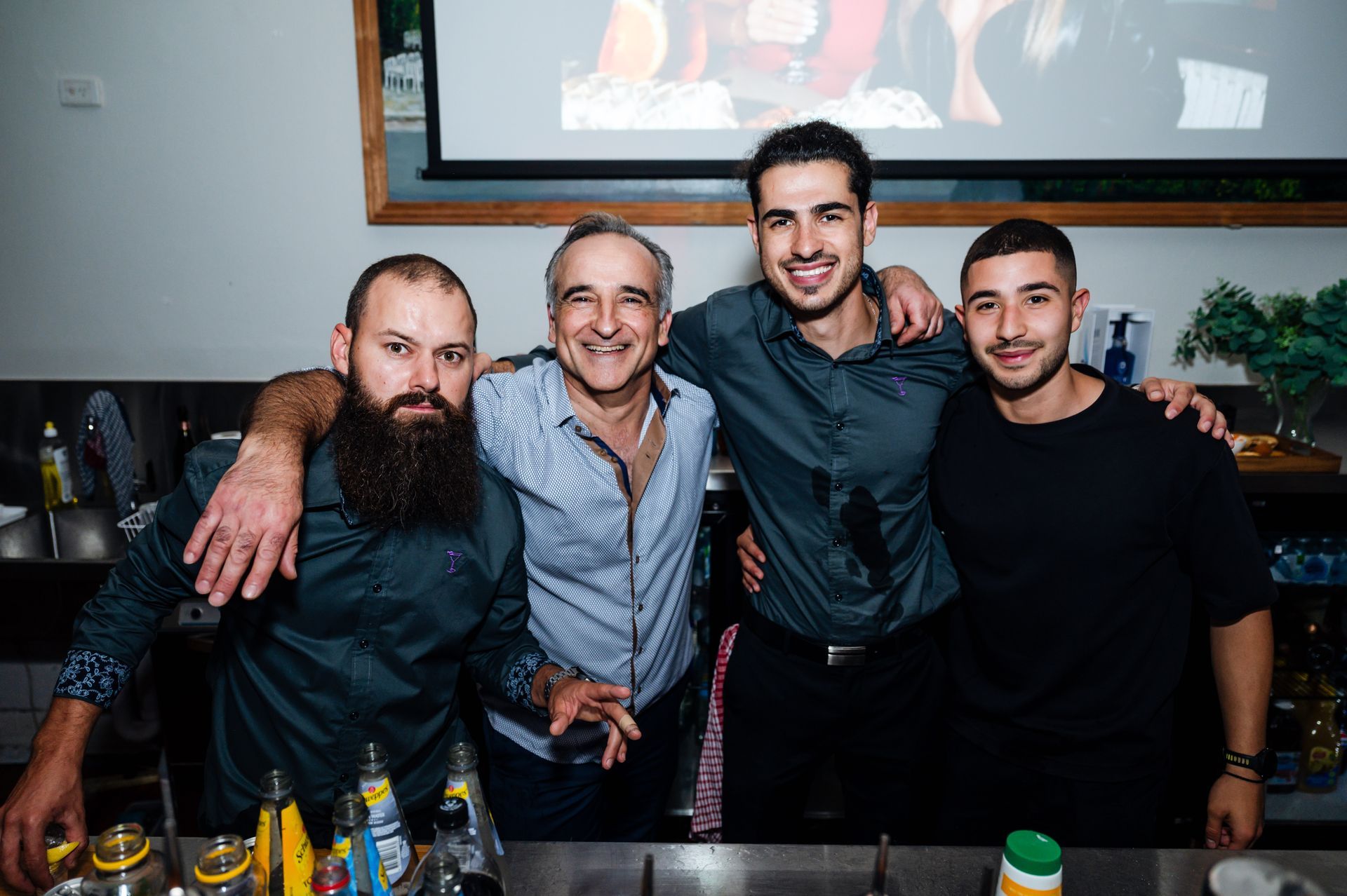 Four men smiling at a bar, posing together with drinks on the counter.