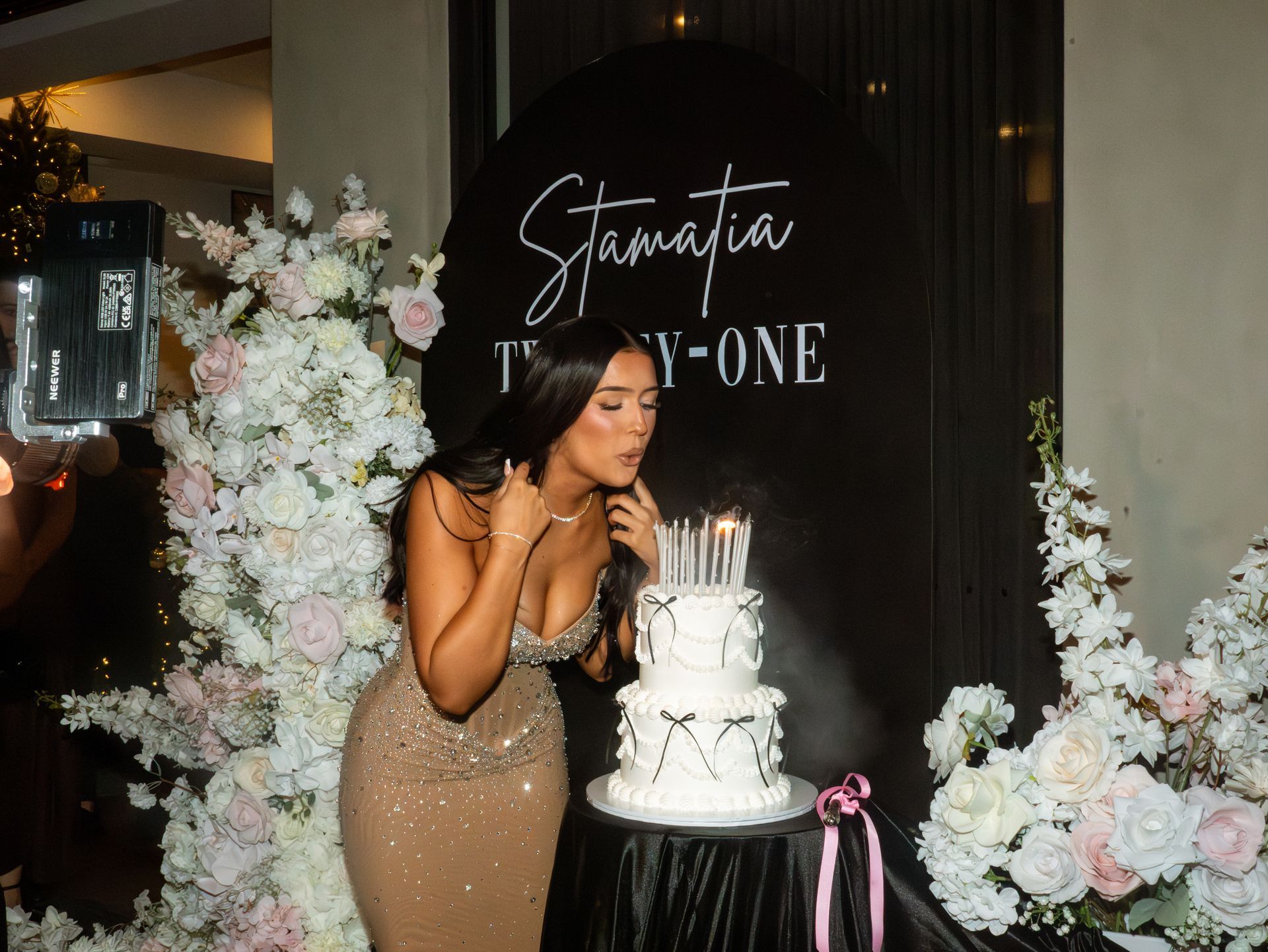 Woman in a gold gown posing beside a white tiered cake at a black-and-white birthday celebration