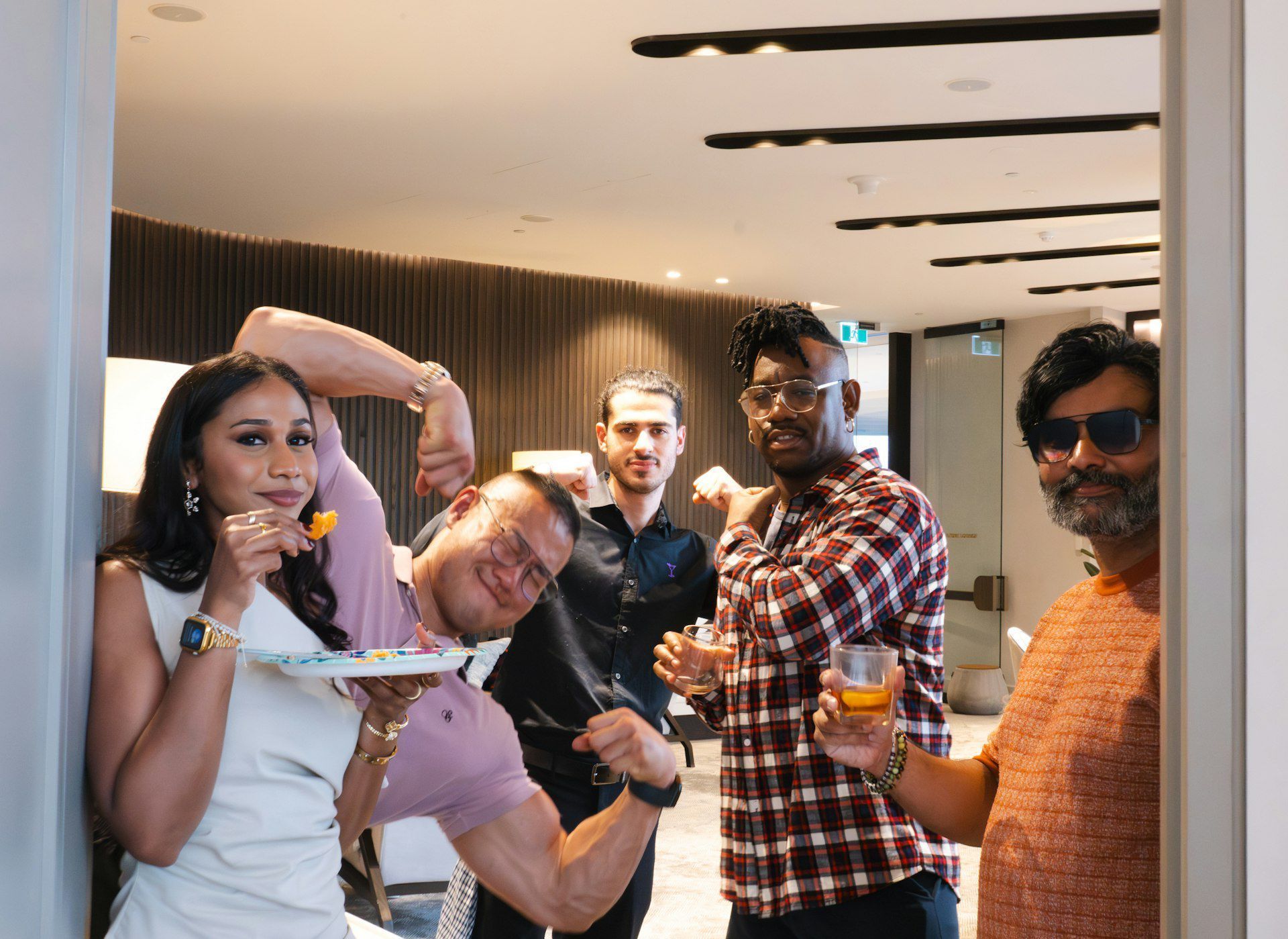 Five people posing and smiling at a casual indoor gathering, one holding a plate of food.