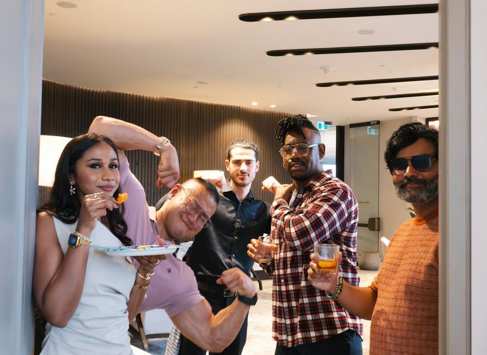Five people posing indoors at a party, smiling and holding drinks in a modern room.