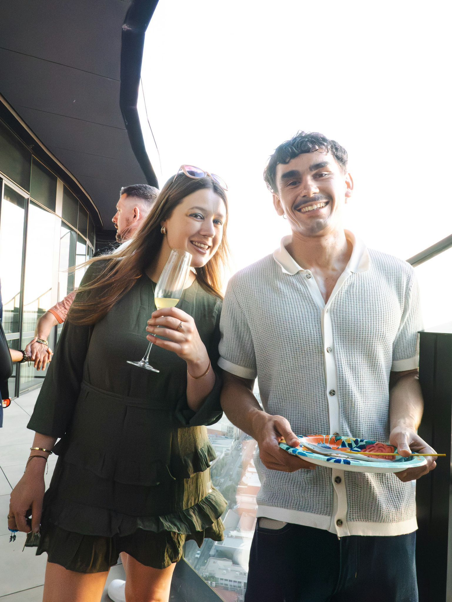 Two people smiling outdoors, holding drinks and a colorful tray of snacks.