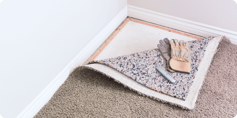 A piece of carpet is laying on the floor next to a pair of gloves.
