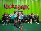 Group of people posing in a gym under a red-and-black “Clockwork” banner on a green wall
