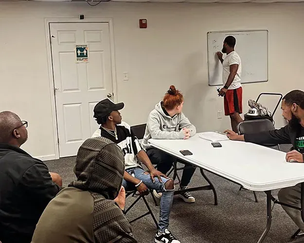 People seated at a table in a meeting room while someone writes on a whiteboard.