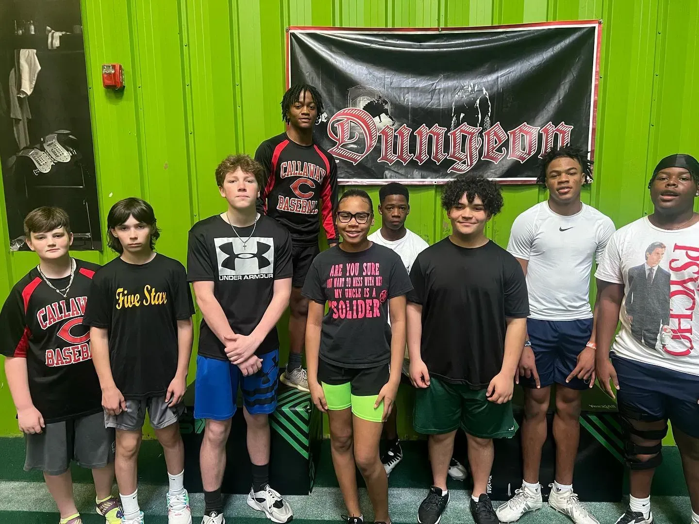 Group of people posing indoors in front of a black banner and bright green wall, wearing casual clothes.