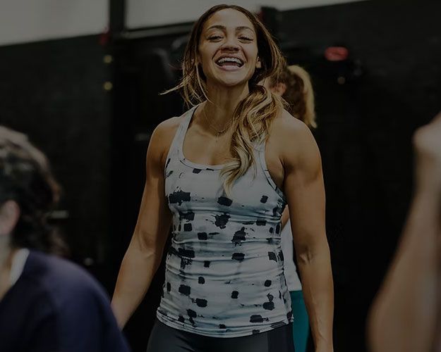 Smiling woman in a gray tank top standing in a gym or workout studio
