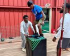 Man balancing on a padded box while two people spot him in an indoor gym.