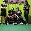 Four people posing indoors on a green carpet in front of a black-and-green backdrop