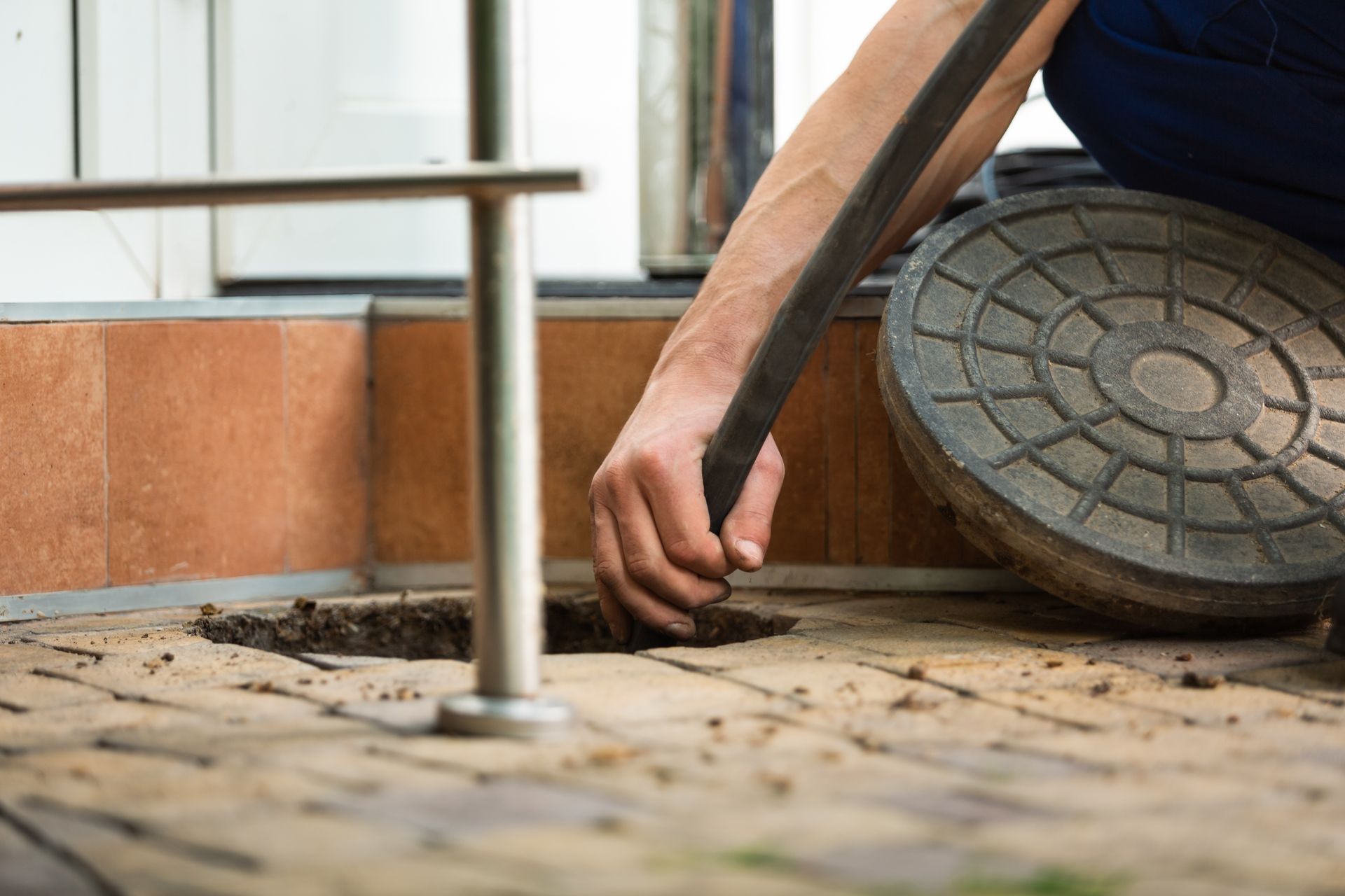 Hand pulling a drain cleaning hose from an open ground cleanout on a paved surface. Hand pulling a drain cleaning hose from an open ground cleanout on a paved surface.