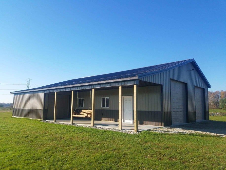 Large metal building with porch and doors, set in a grassy field under a blue sky.