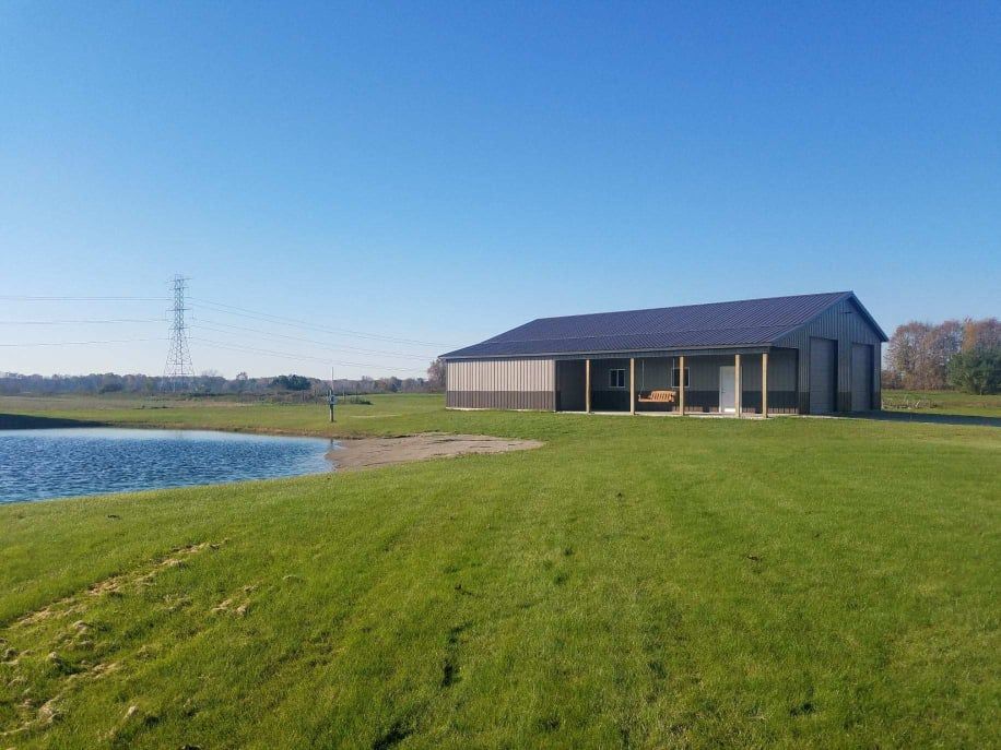 Grassy field with a pond and a building with a screened porch under a blue sky. Power lines are visible in the distance.